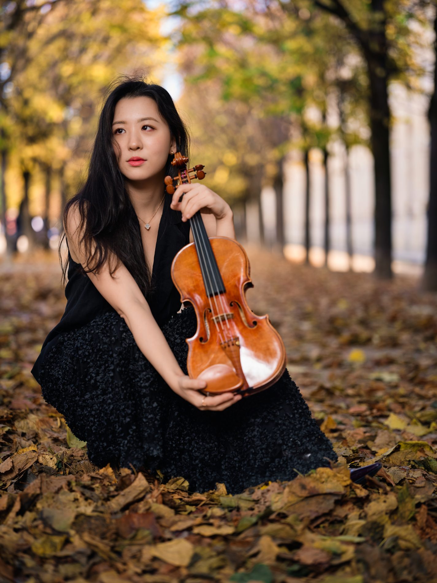 Anna Lee seated among autumn leaves with her violin