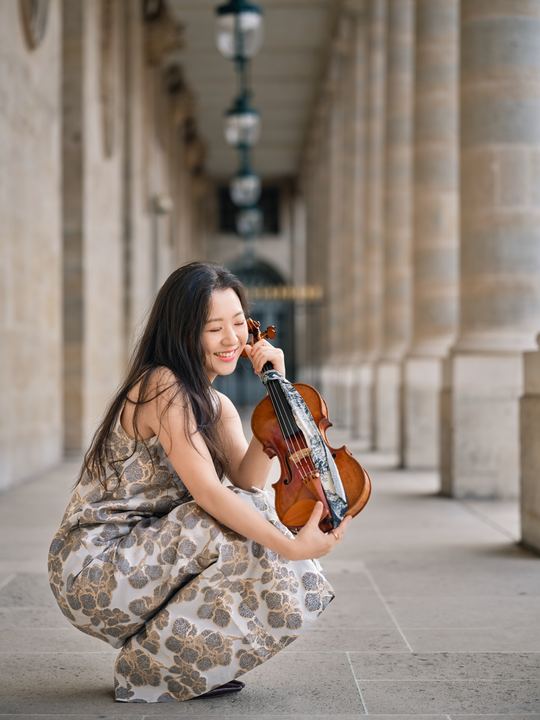 Anna Lee holding her violin in a patterned gown
