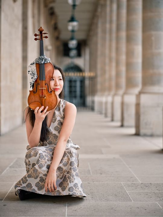 Anna Lee seated with her violin in a patterned gown