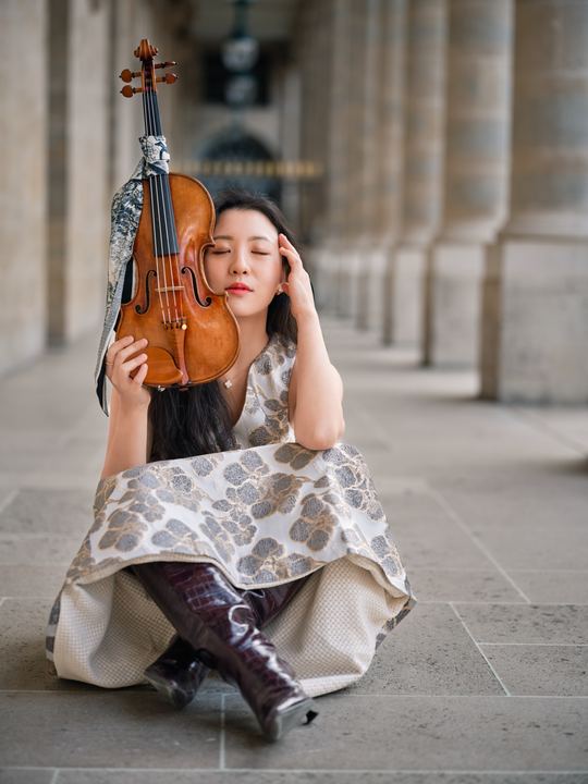 Anna Lee with her violin beneath a colonnade
