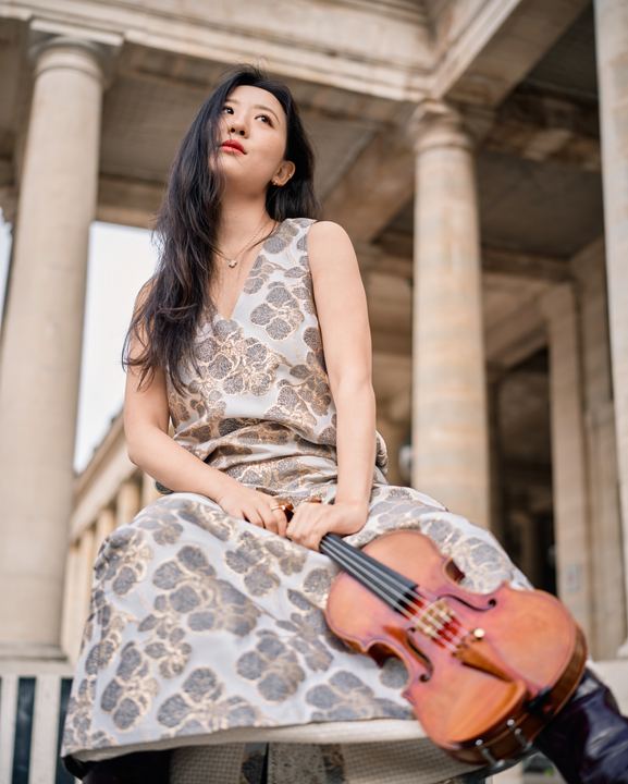 Anna Lee with her violin in a patterned gown