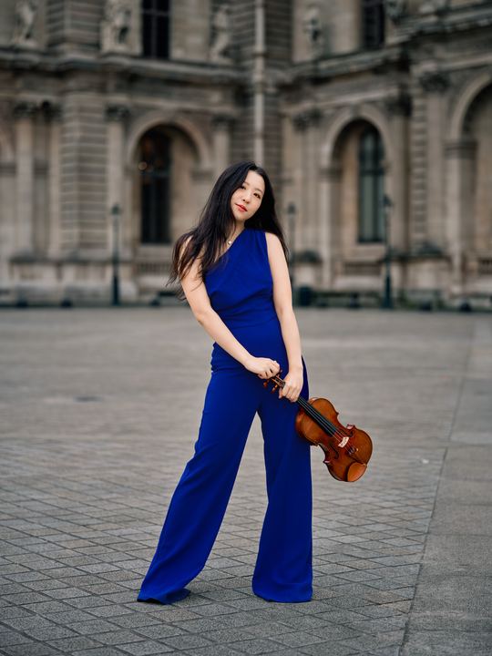 Anna Lee in a royal blue dress with her violin at the Louvre