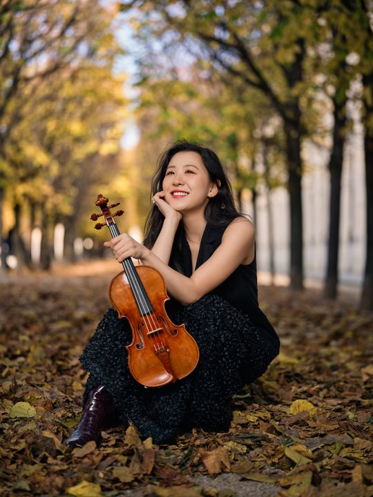 Portrait of Anna Lee seated among autumn leaves with her violin